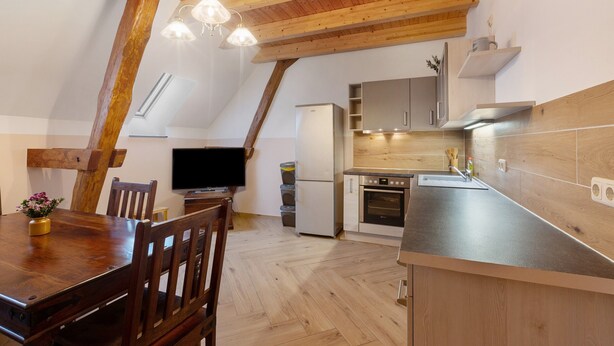 A kitchen with wooden beams, a dining table, chairs, a refrigerator, an oven, and a TV.