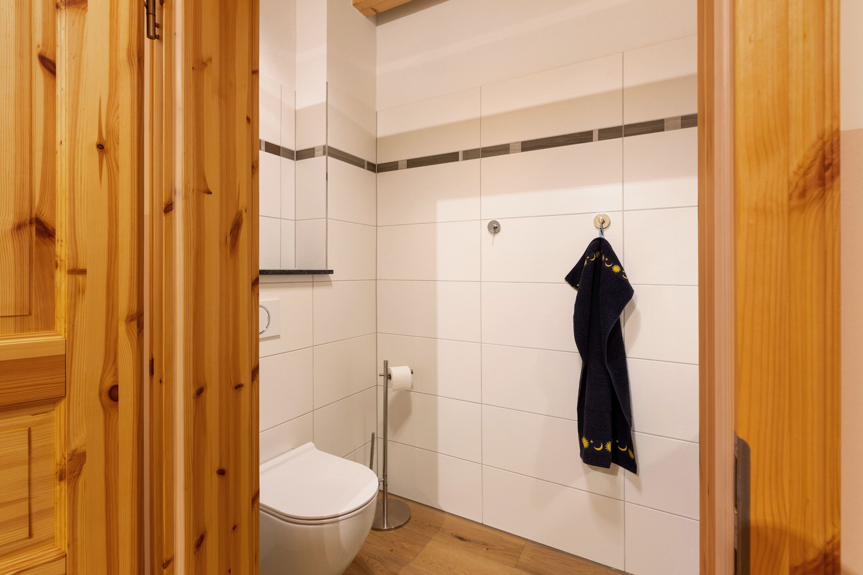 Eine Holztür, eine weiße Toilette, ein Handtuchhalter mit Handtuch und ein Toilettenpapierhalter.