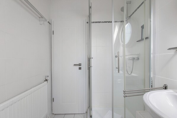 Une salle de bain moderne avec une douche à parois de verre, un lavabo blanc et une porte donnant sur une autre pièce.