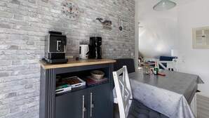 Et køkken med en murstensvæg, et ur, en kaffemaskine og et spiseområde med et bord og stole.