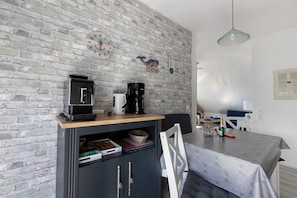 Une cuisine avec un mur en briques, une horloge, une machine à café et un coin repas comprenant une table et des chaises.