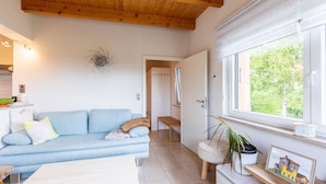 Un salón moderno con un sofá azul, techo de madera, ventana con vistas, una mesita y una planta en maceta.