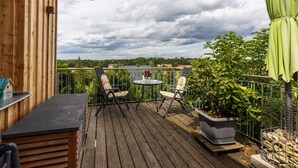 Una terraza de madera con una mesa, sillas, una planta en maceta y vistas al paisaje.