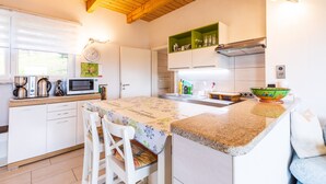 Una cocina con armarios blancos, techo de madera, microondas, hervidor y un estante verde.