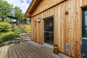 Een houten gebouw met een glazen deuropening, een houten terras en een klein buitenzitgedeelte met een groene parasol.