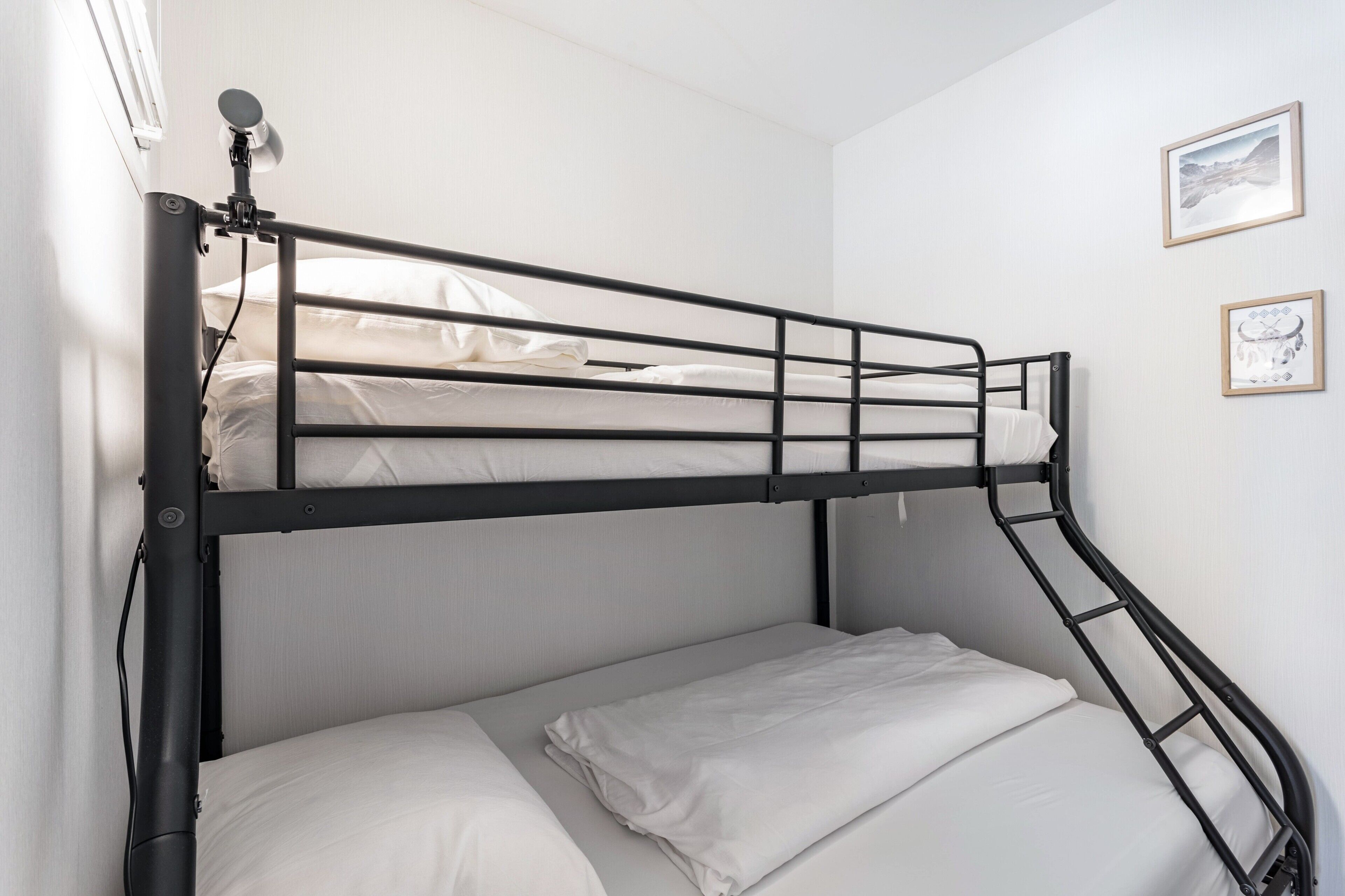 Un lit superposé avec une échelle, du linge de lit blanc et deux tableaux encadrés accrochés au mur.