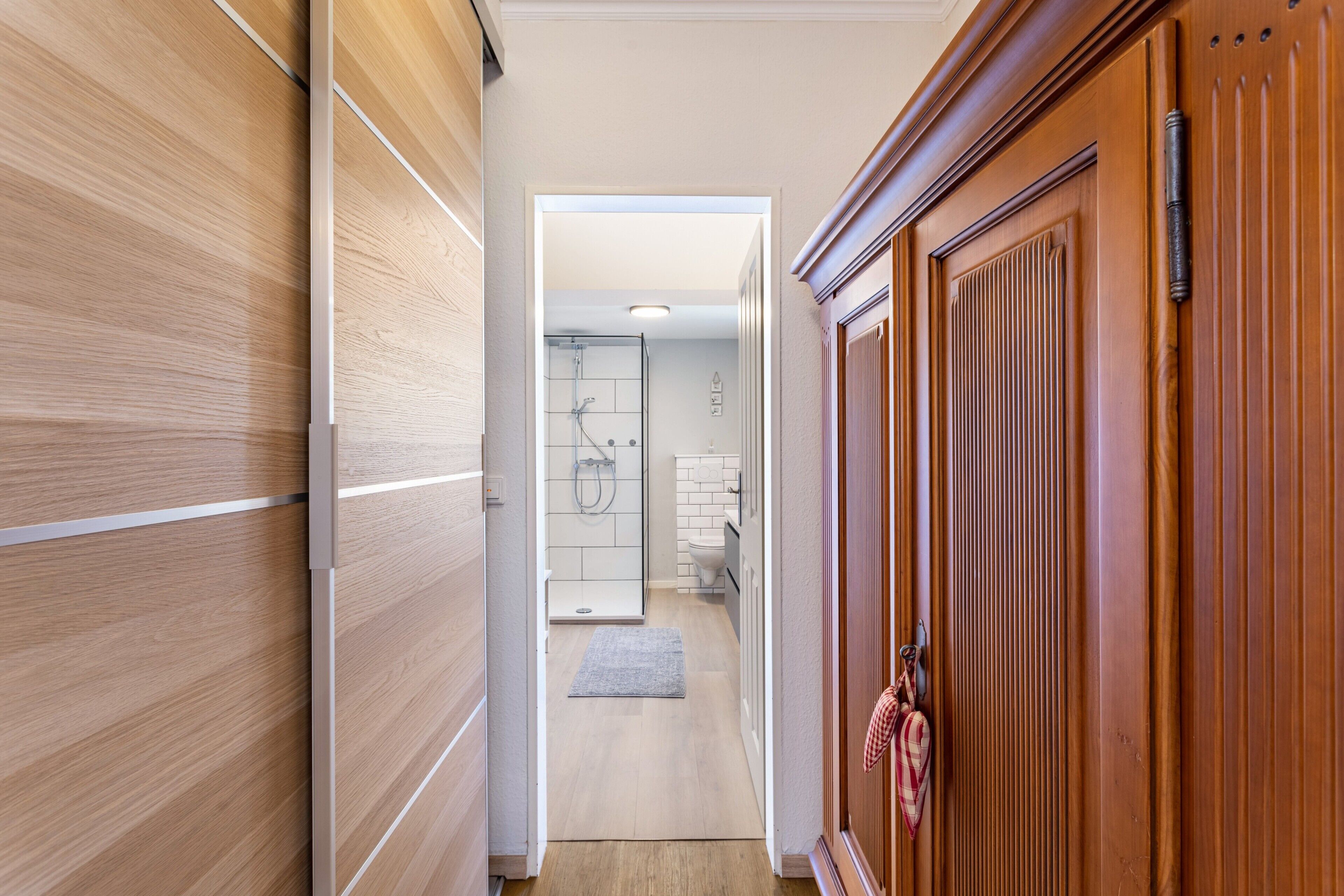 Un couloir menant à une salle de bain équipée d’une douche, de toilettes et d’un lavabo.