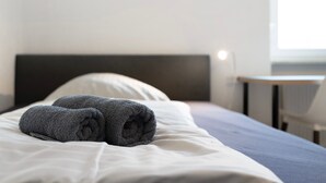 Ein Bett mit weißer Bettwäsche und zwei aufgerollten Handtüchern.