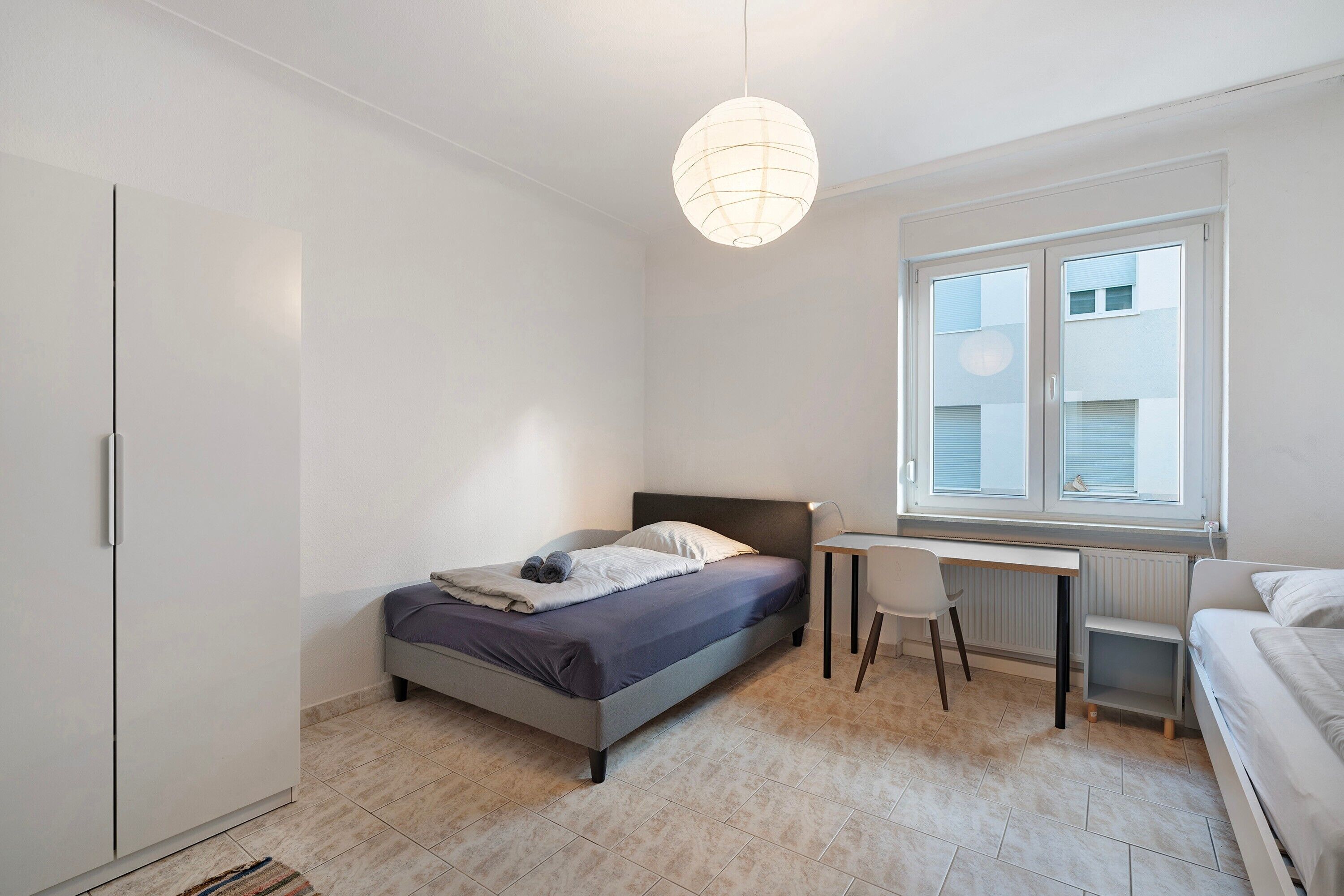 Un dormitorio con cama, escritorio, silla, armario y ventana con persianas.