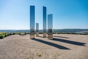 Une série de structures hautes et étroites, agrémentées de panneaux d’information, est disposée sur un sol de gravier, avec un ciel dégagé et des collines lointaines en arrière-plan.