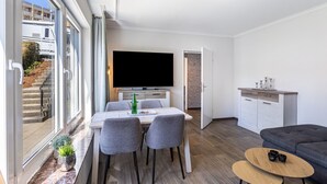 A modern living room with a flat-screen TV, a dining area with a table and chairs, a sofa, and a kitchen area with cabinets. - Holiday Apartments Löwenstein FeWo 1 with Private Terrace & Garden and Wi-Fi (Willingen (Upland))