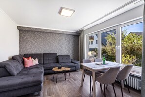 Una sala de estar moderna con un sofá modular, una mesa de comedor con sillas y grandes ventanales que ofrecen vistas al exterior.