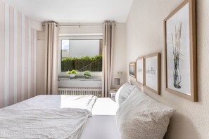 Habitación de hotel con cama, ventana con cortinas y vistas a zonas verdes, además de cuadros en la pared.