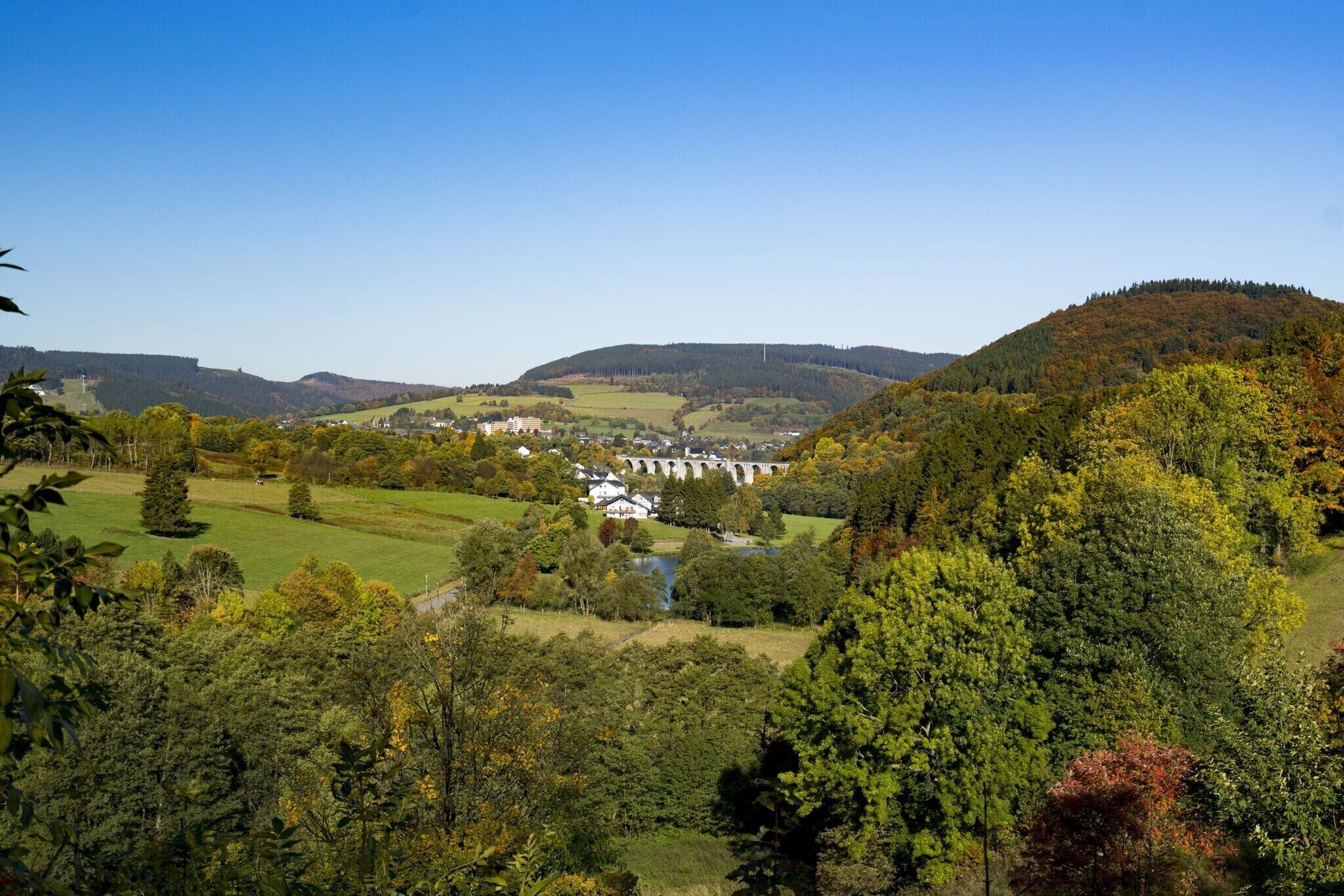 Un paysage rural avec un pont, des bâtiments et une colline.
