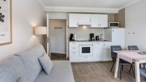 A compact living space with a kitchenette, a sofa, a dining table, and a lamp. - Holiday Apartments Löwenstein FeWo 3 with Private Terrace, Shared Garden and Wi-Fi (Willingen (Upland))