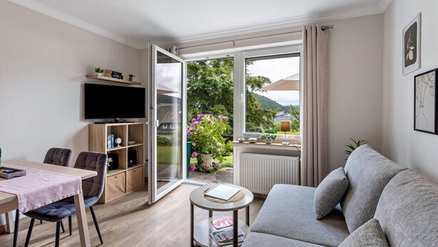A modern living room with a sofa, a TV, a dining table, and a bookshelf. - Holiday Apartments Löwenstein FeWo 3 with Private Terrace, Shared Garden and Wi-Fi (Willingen (Upland))