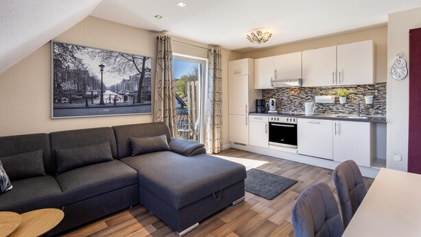 A modern apartment with a sofa, dining table, kitchen, and a large window.
