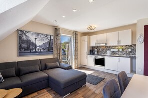 Eine moderne Wohnung mit Sofa, Esstisch, Küche und einem großen Fenster.