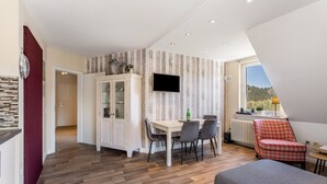 A modern living room with a dining area, a TV mounted on the wall, and a view of the outdoors.