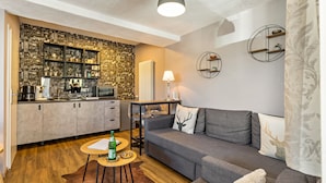 A modern living space with a kitchen, grey sofa, and a patterned wall.