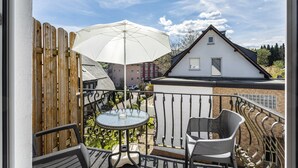 A balcony with a table, chairs, and a white umbrella.