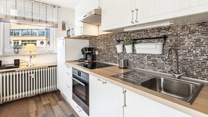A modern kitchen with white cabinets, a brick backsplash, and a large stainless steel sink.