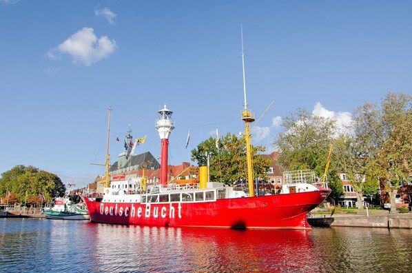A red boat named 'Deutsche Bucht' docked at a harbor with a lighthouse and buildings in the background.