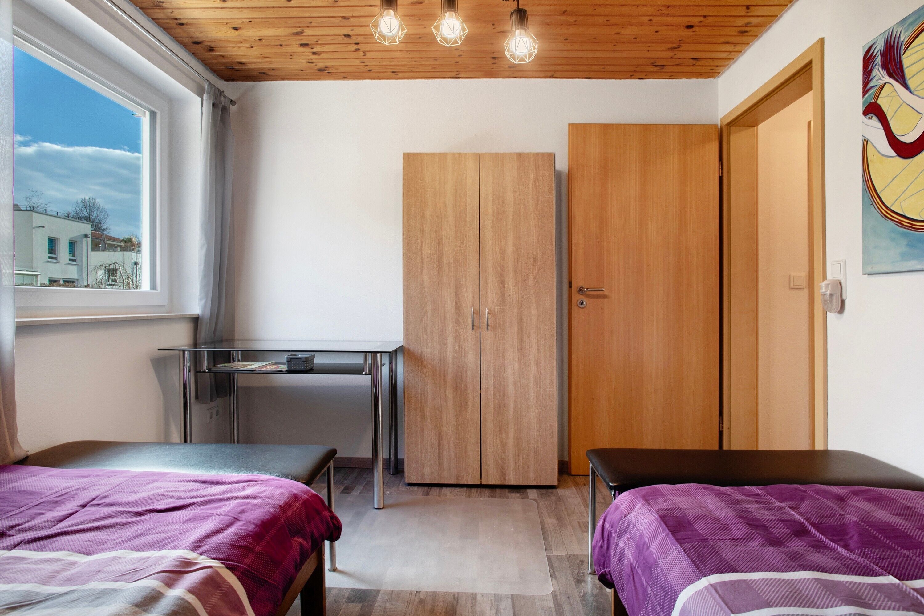 Une chambre avec un lit, un bureau, une armoire et une fenêtre donnant sur des immeubles.