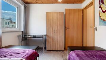A room with a bed, a desk, a wardrobe, and a window with a view of buildings.