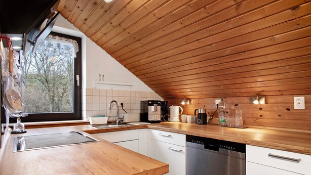 A modern kitchen with wooden ceiling, white cabinetry, stainless steel dishwasher, and various appliances.