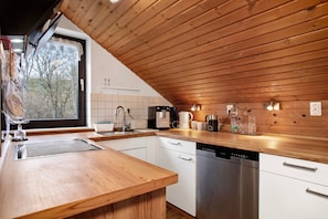A modern kitchen with wooden ceiling, white cabinetry, stainless steel dishwasher, and various appliances.
