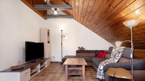 A modern living room with a television, sofa, coffee table, and a wooden ceiling.