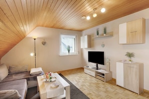 A cozy living room with a wooden ceiling, a TV, a cabinet, and a window.