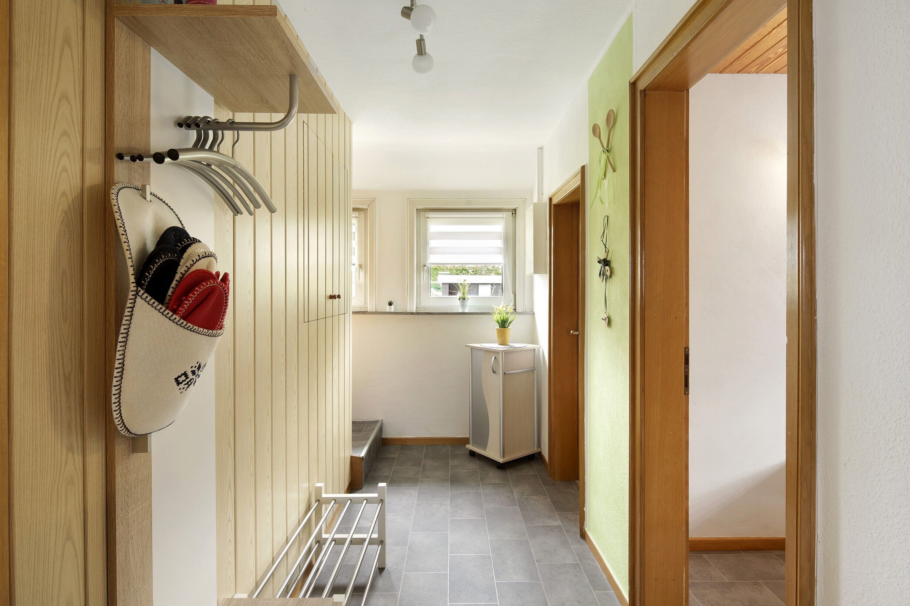 Ein schmales Entree mit Kleiderhaken, einem kleinen Schrank und einem Fenster mit Blick auf Grünflächen.