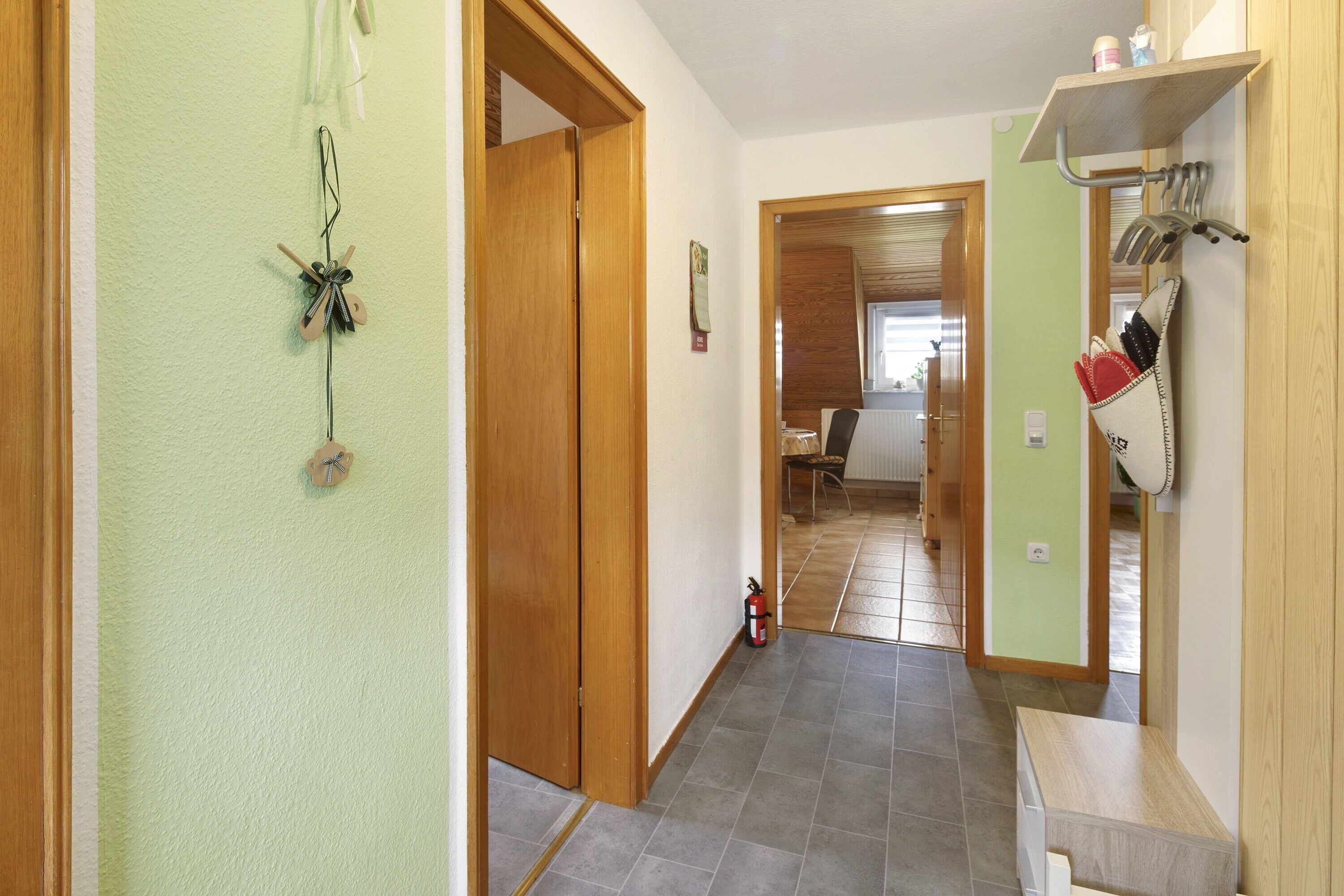 A hallway with a wooden door, a fire extinguisher, and a shelf with kitchen utensils.