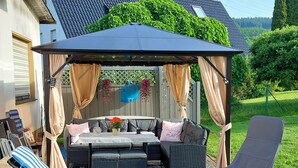 Un espace extérieur abrité, aménagé avec une table, des chaises et un kiosque.