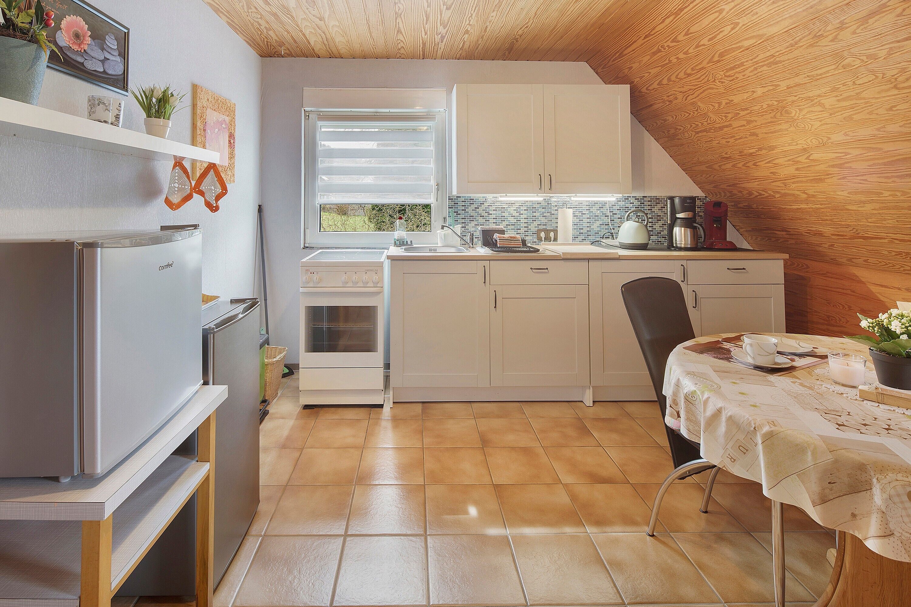 Une cuisine de taille réduite, avec des meubles blancs, un réfrigérateur en acier inoxydable et une table à manger recouverte d’une nappe.