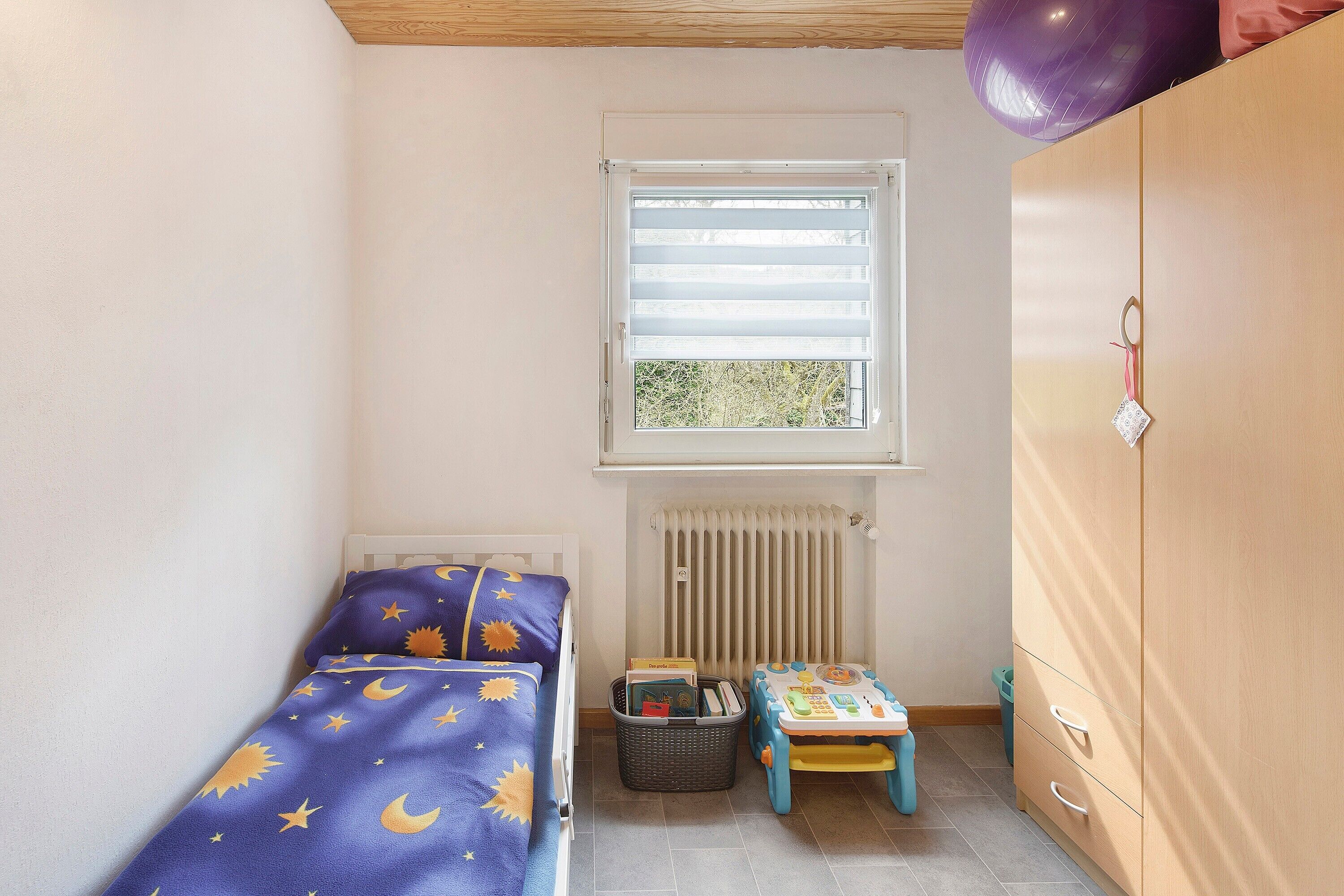 Une chambre d’enfant avec un lit, une petite table, un radiateur et une armoire.