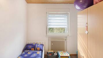 Une chambre d’enfant avec un lit, une petite table, un radiateur et une armoire.