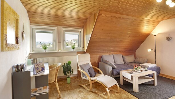 Une pièce confortable de style loft, avec un plafond en bois, un canapé, un fauteuil à bascule, une petite table et une fenêtre donnant sur un beau paysage.