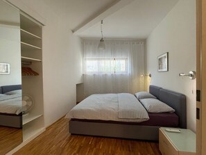 Quarto com cama, mesa de cabeceira, guarda-roupa, janela com cortinas e luminária no teto.