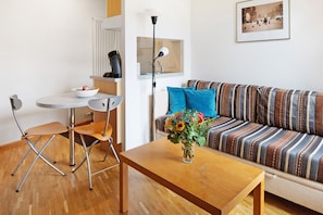 Ett modernt vardagsrum med en randig soffa, ett litet runt bord, en stol, en vas med blommor, ett element, en inramad tavla och en lampa.