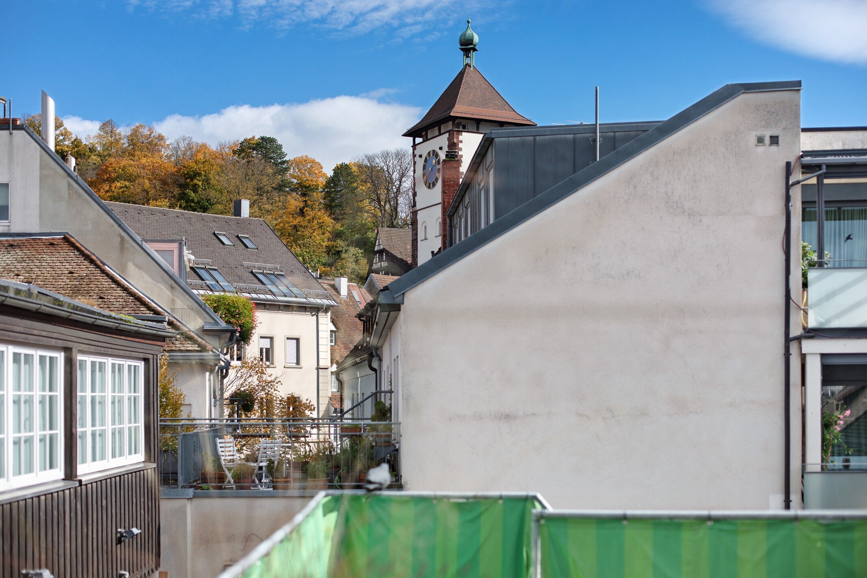 Un bâtiment doté d’une tour horlogée, d’un balcon et d’une barrière de protection verte.