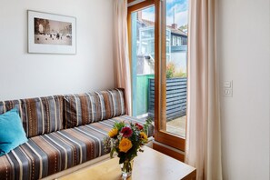 Una habitación con un sofá a rayas, un jarrón con flores y una ventana con cortinas.