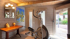 A wooden interior with a stationary bike, a mirror with lights, a table with a statue, and a painting. - Apartment 'Standfuss' with Private Terrace, Garden, and Wi-Fi (Dausenau)