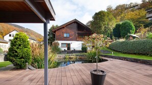 A wooden deck with a potted plant, a pond, and a house with a sloped roof. - Apartment 'Standfuss' with Private Terrace, Garden, and Wi-Fi (Dausenau)