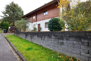 Een houten huis met twee verdiepingen, een stenen keerwand, een kleine tuin en een verharde oprit.