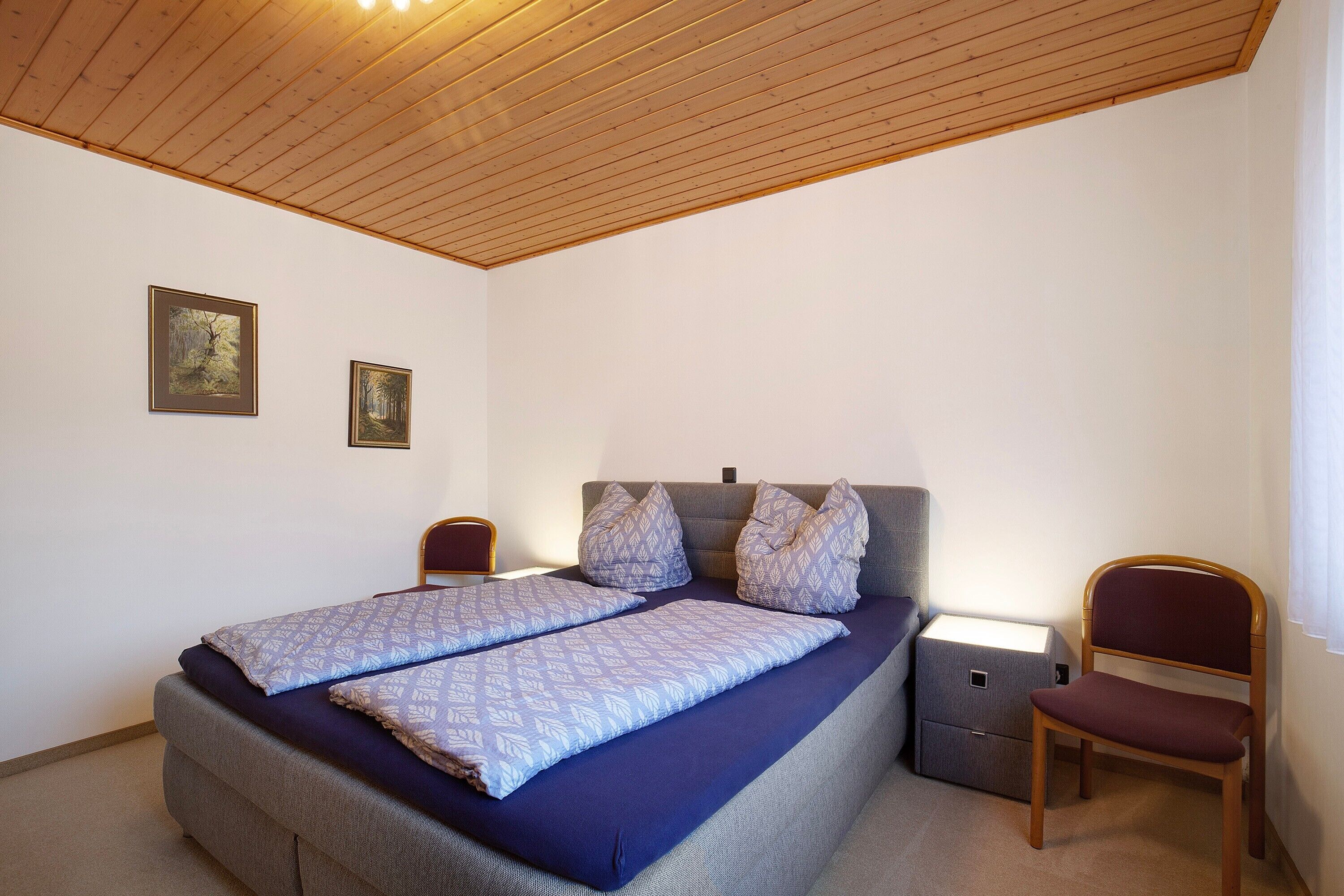 A bedroom with a bed, two nightstands, a chair, and two framed pictures on the wall.