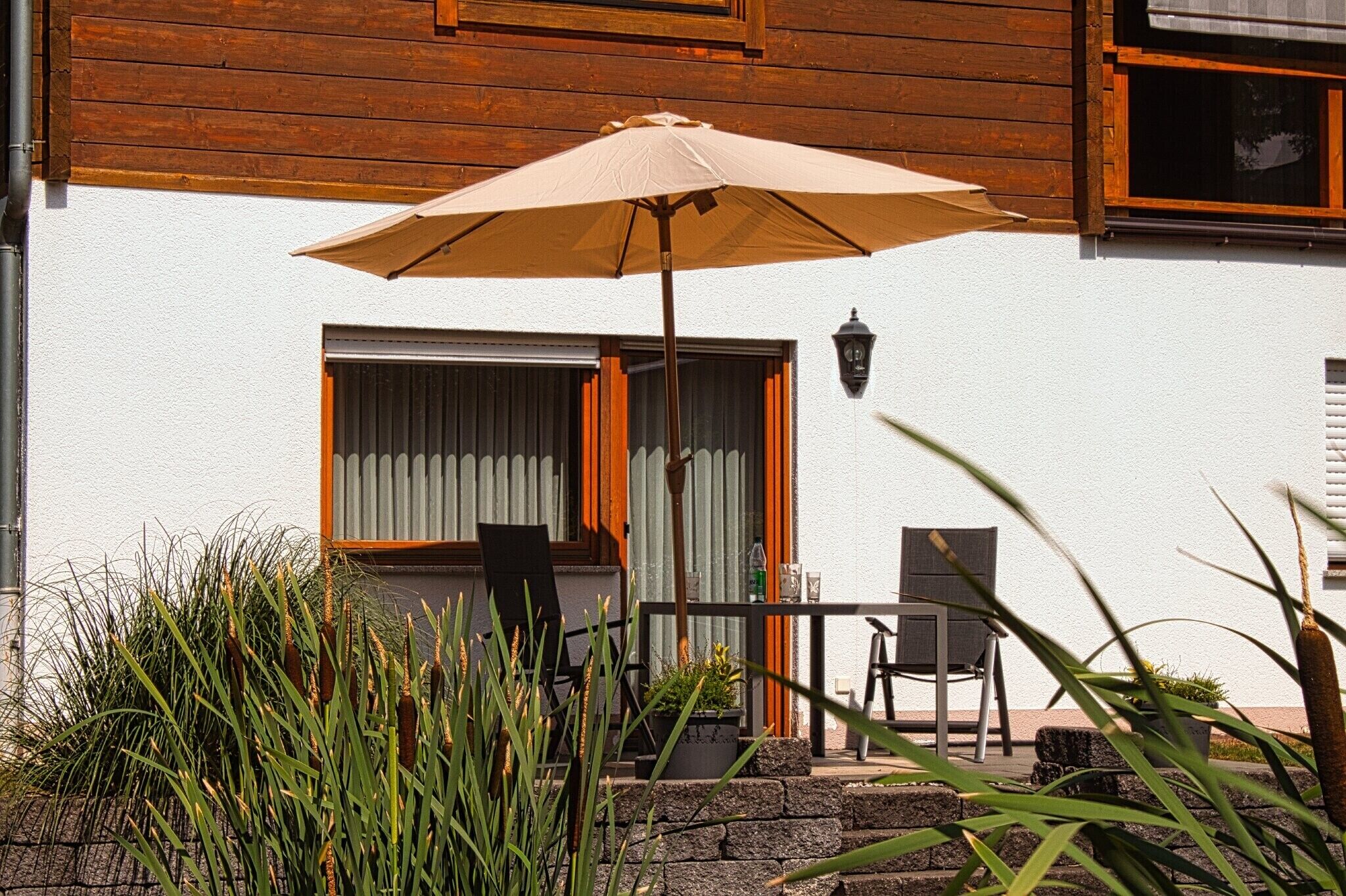 Une terrasse avec une table et des chaises, un parasol et une fenêtre avec des rideaux.