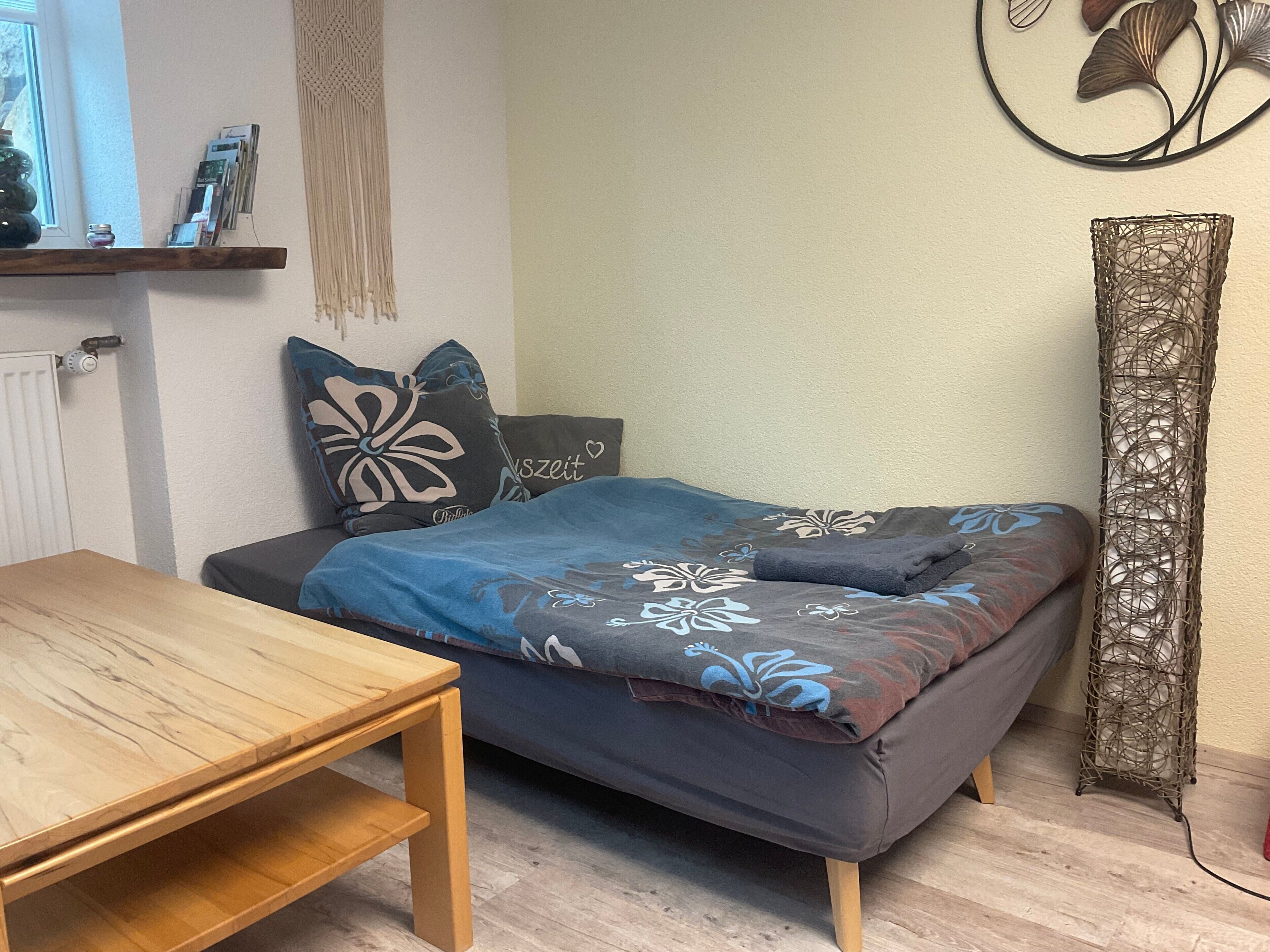 Une chambre à coucher comprenant un lit, une table en bois, une décoration murale en macramé et un élément décoratif mural.